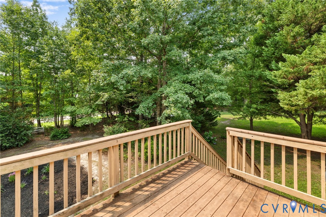 Wood-tone deck with railing and stairs, surrounded by mature trees and natural landscaping