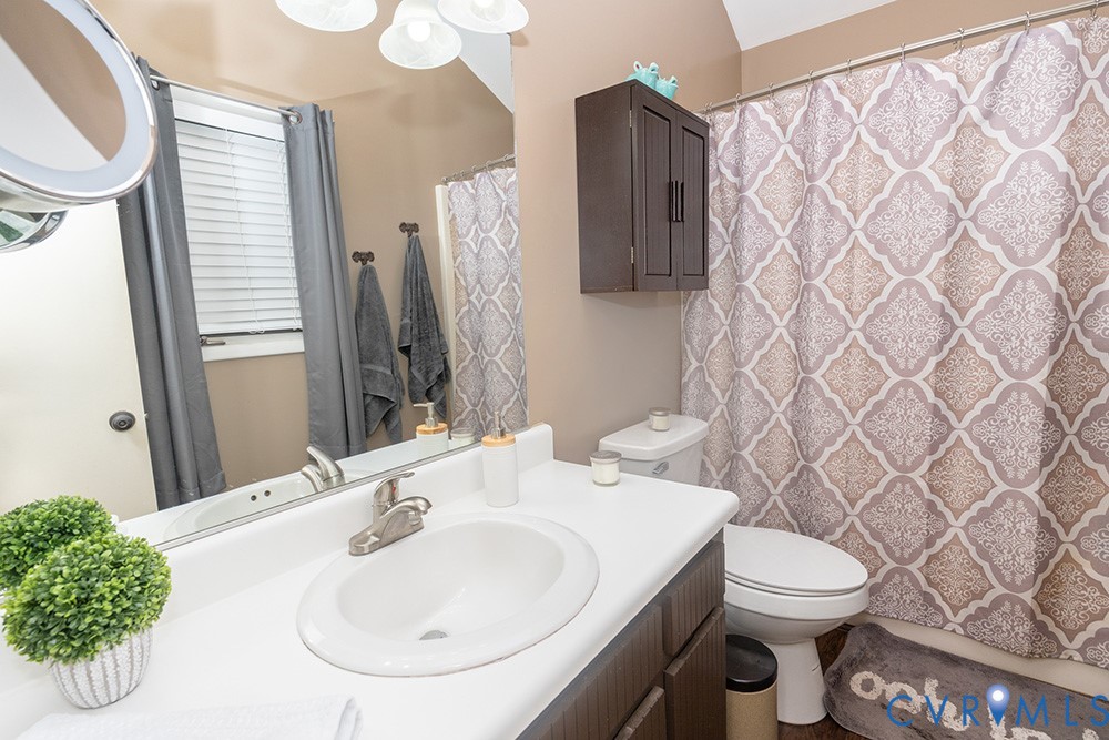 White countertop with integrated sink, dark wood-finish vanity, wall-mounted storage cabinet, and a functional toilet