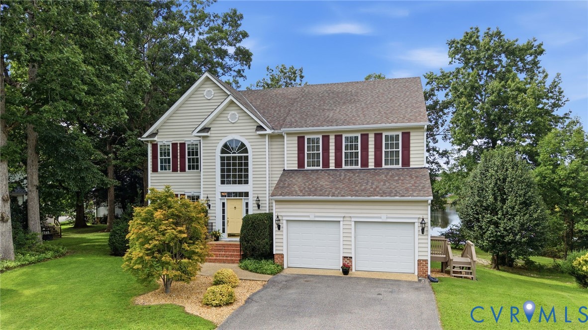 Beautiful waterfront two-story home with mature landscaping, a two-car garage, and a welcoming front entrance.