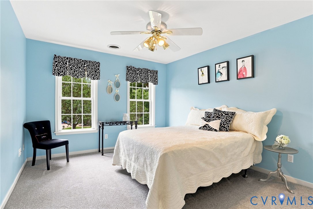 Bright secondary bedroom with two windows, ceiling fan, and generous space for furnishings.