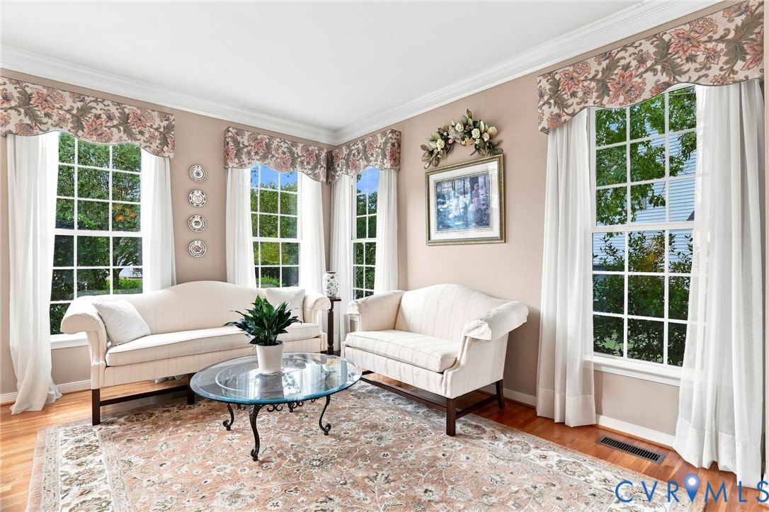 Bright formal living room features hardwood floors, crown molding, and an abundance of natural light from multiple windows.