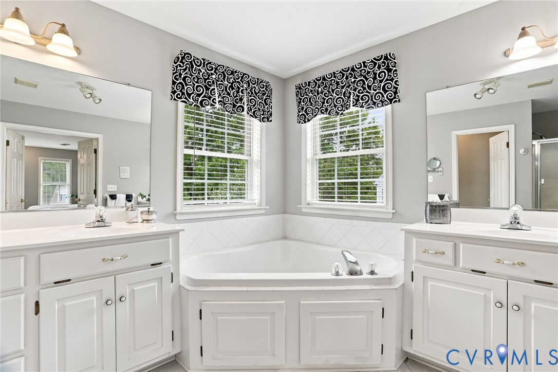 Corner soaking tub is framed by two windows and flanked by separate vanities for added functionality.