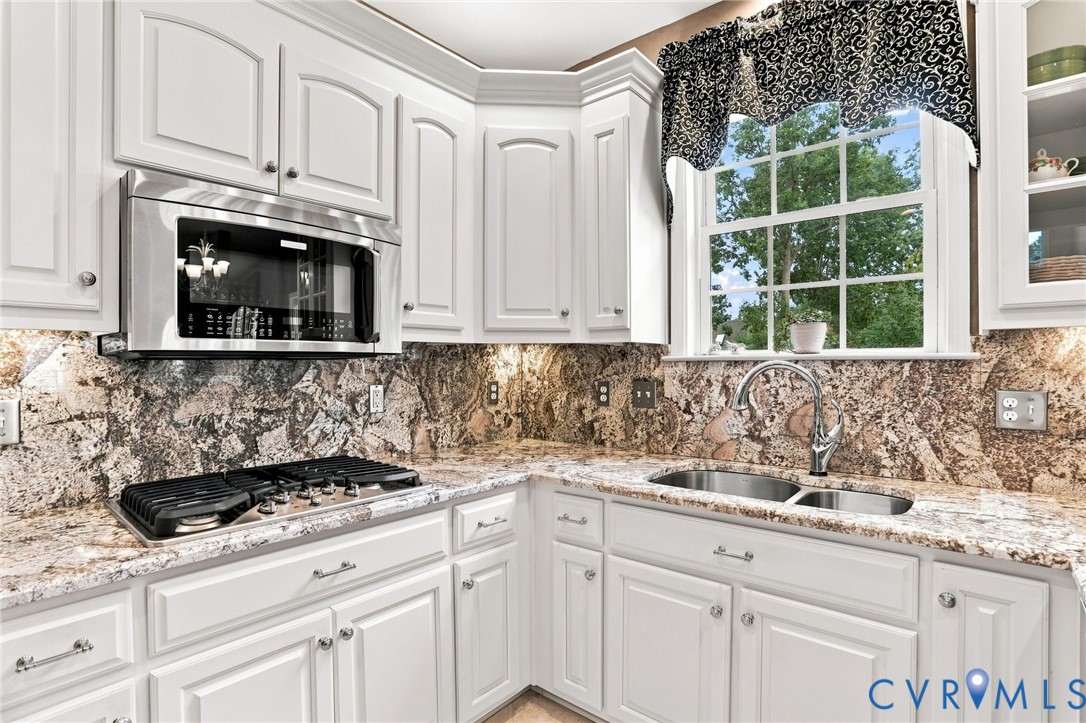 Granite countertops and backsplash complement the white cabinetry, stainless steel appliances, and gas cooktop.