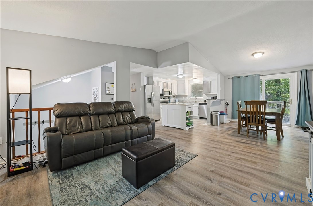 Angled ceilings, wood-finish flooring, white kitchen cabinetry, kitchen island with open shelving, and a sliding glass door