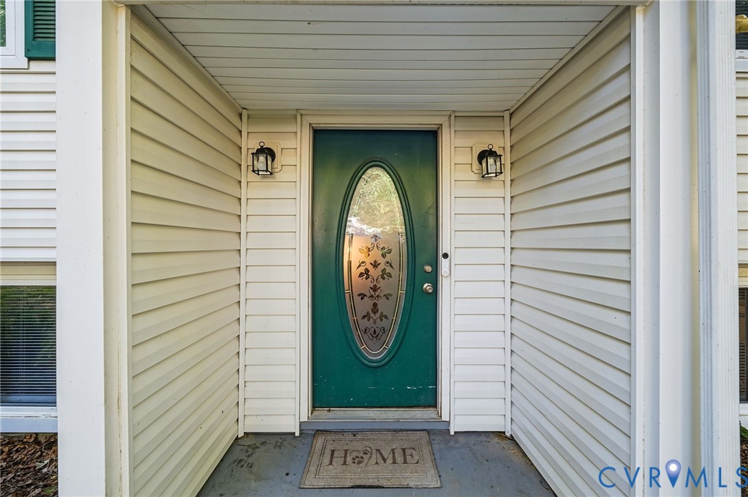 Welcoming entry featuring a distinctive oval glass-panel door in forest green, flanking sidelights with decorative sconces, horizontal lap siding in cream, and a covered portico with coffered ceiling detail