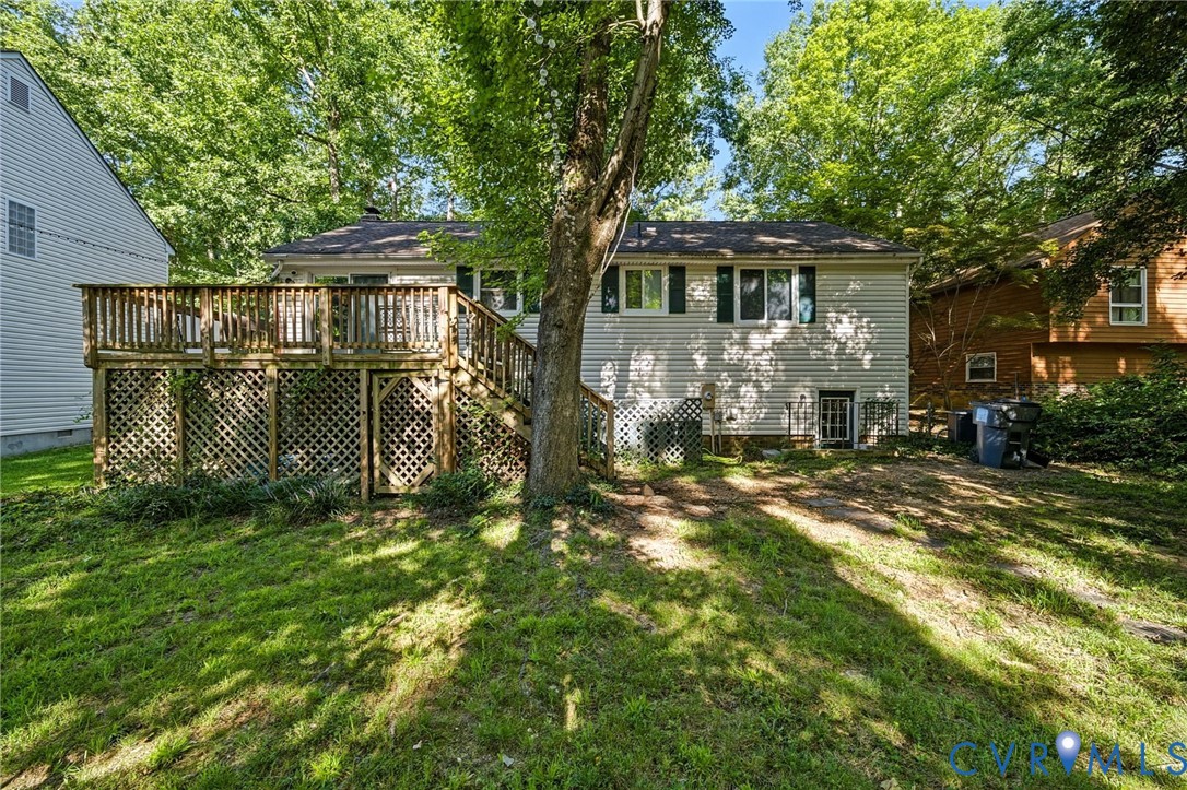Rear exterior with a wood-finish deck, lattice skirting, and a sloped grass lawn