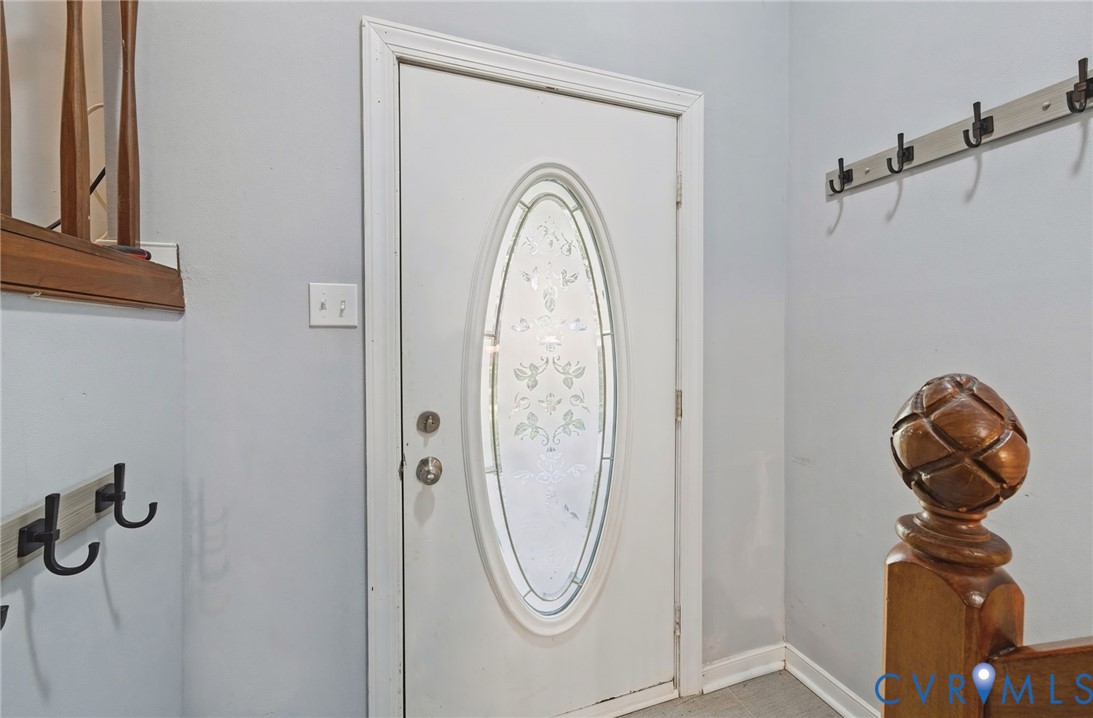 Entry door with decorative oval glass insert, a coat rack with multiple hooks, and a wood newel post