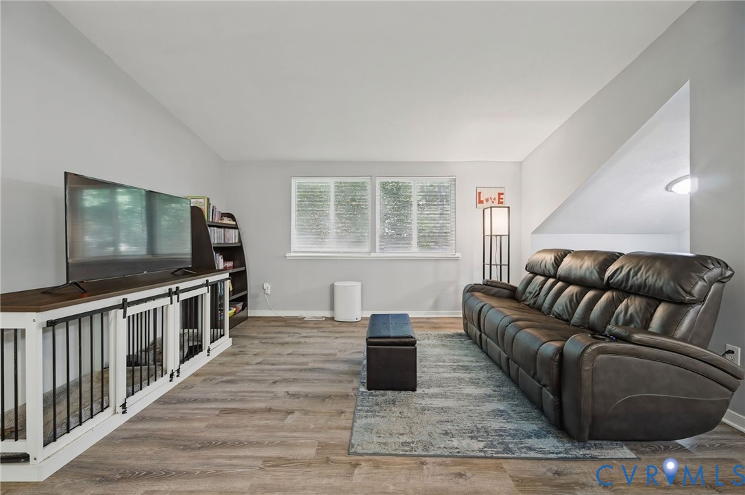 Wood-finish flooring throughout, light gray wall color, dual pane window, built-in shelving, vaulted ceiling