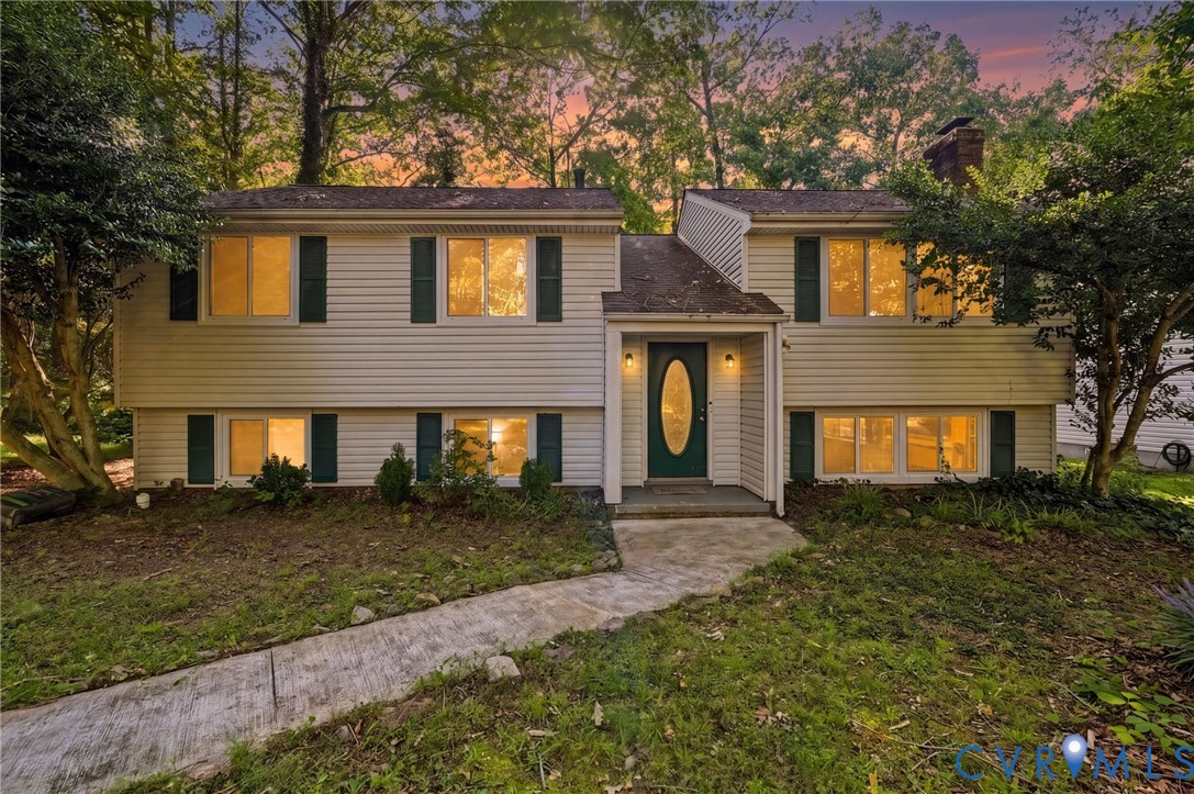 Split-level home featuring light-toned siding, dark green shutters, and a prominent front entry with a dark green door