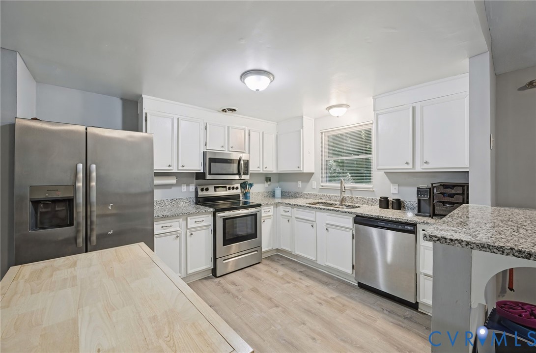 Kitchen featuring stainless steel appliances, white cabinetry, speckled countertops, wood-finish flooring, and a double basin sink