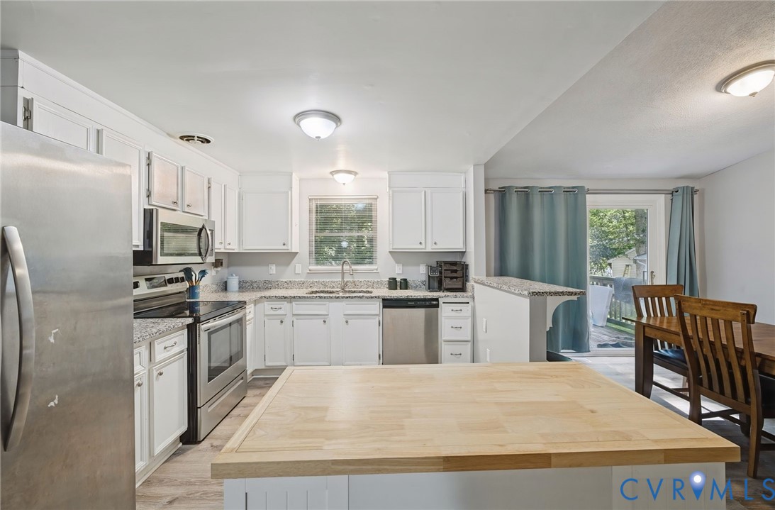 Kitchen featuring a wood-finish island, white cabinetry, stainless steel appliances, and a pass-through counter