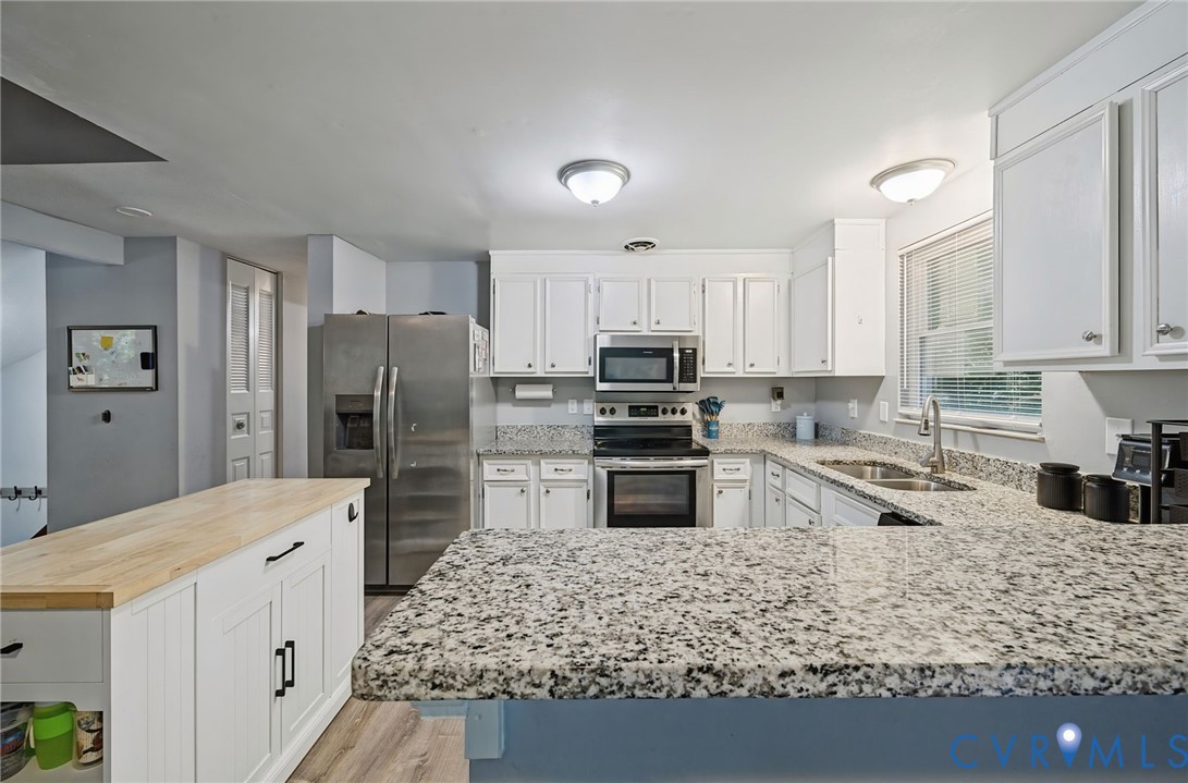Kitchen featuring white cabinetry, stainless steel appliances, granite countertops, a double basin sink, and a center island with wood-finish top