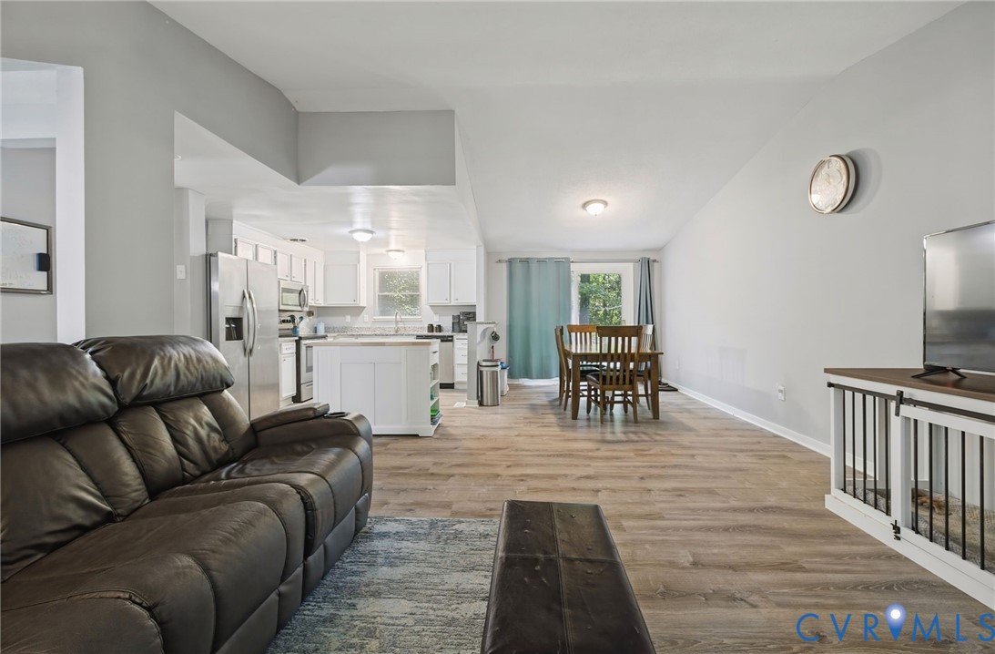 Open-concept living space featuring wood-finish flooring, white cabinetry, a kitchen island, and stainless steel appliances