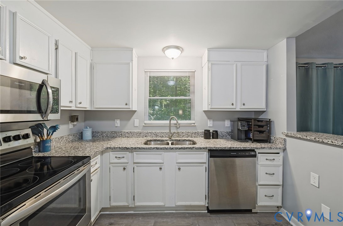 White cabinetry, stainless steel appliances, speckled countertops, wood-finish flooring, and a double basin sink