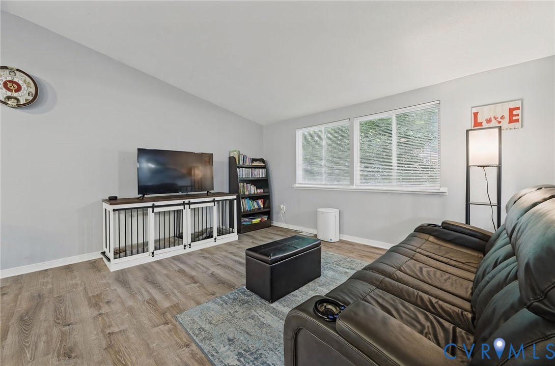 Vaulted ceiling, wood-finish flooring, light gray wall color, multiple large windows, and built-in shelving