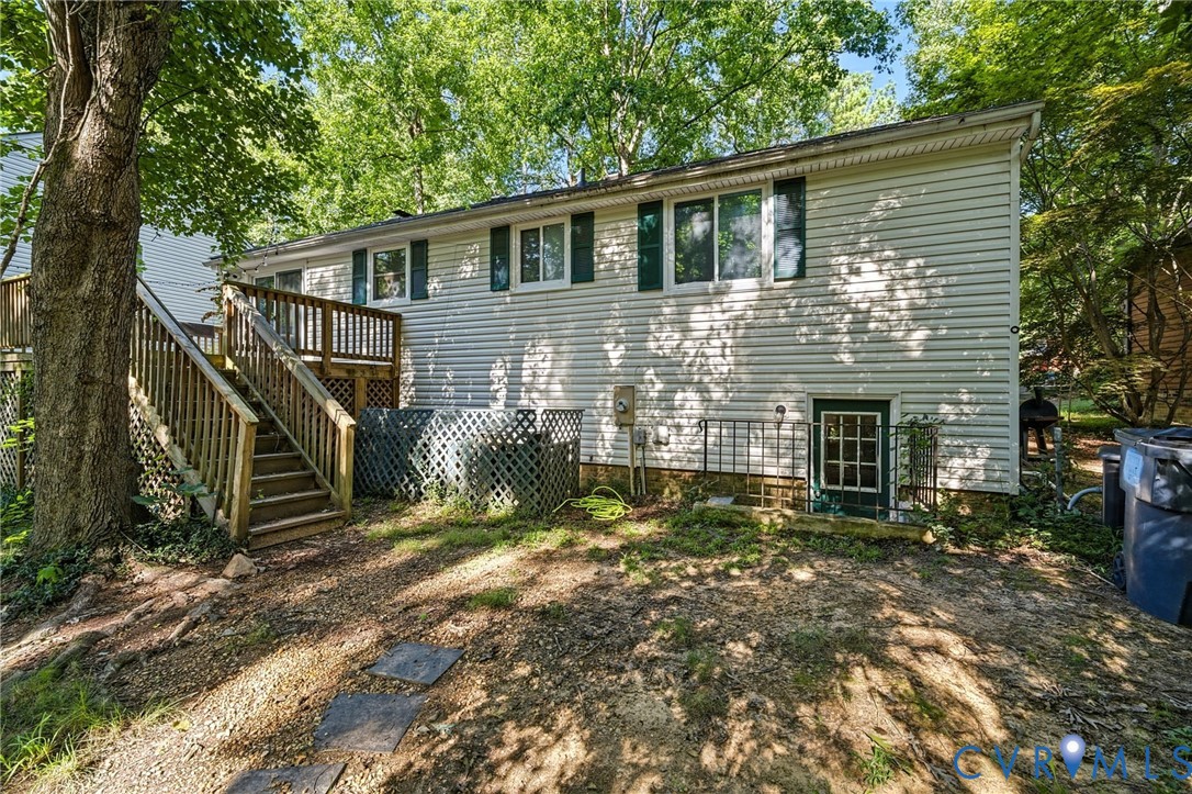 Rear exterior featuring vinyl siding, multiple windows with shutters, a wooden deck with railing and stairs, and a ground-level exterior door