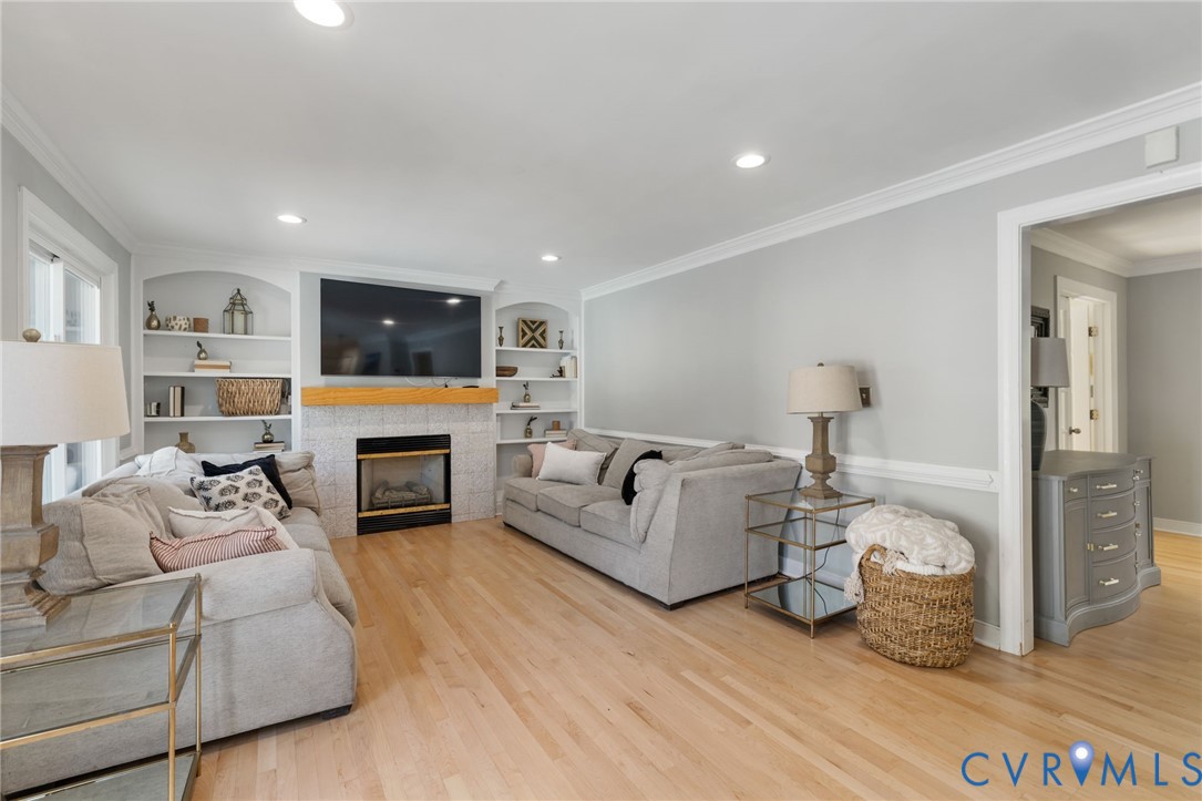 Light wood-finish flooring, built-in shelving, fireplace with tile surround, recessed lighting, and crown molding