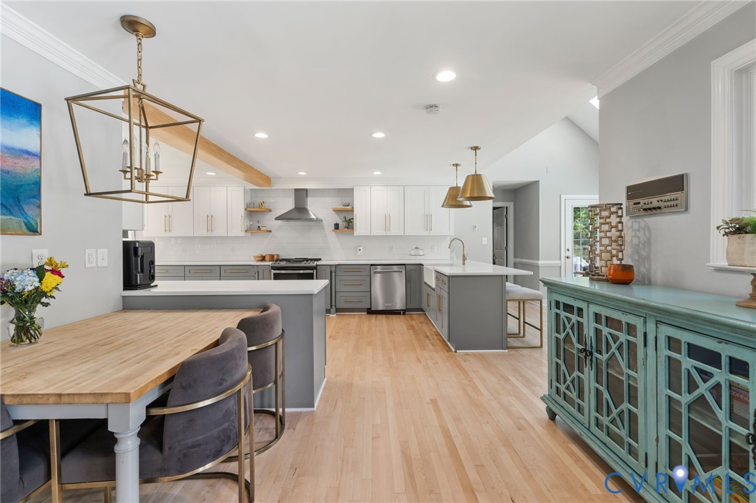 Open-concept kitchen with white and gray cabinetry, a central island featuring a farmhouse sink, stainless steel appliances, and wood-finish flooring