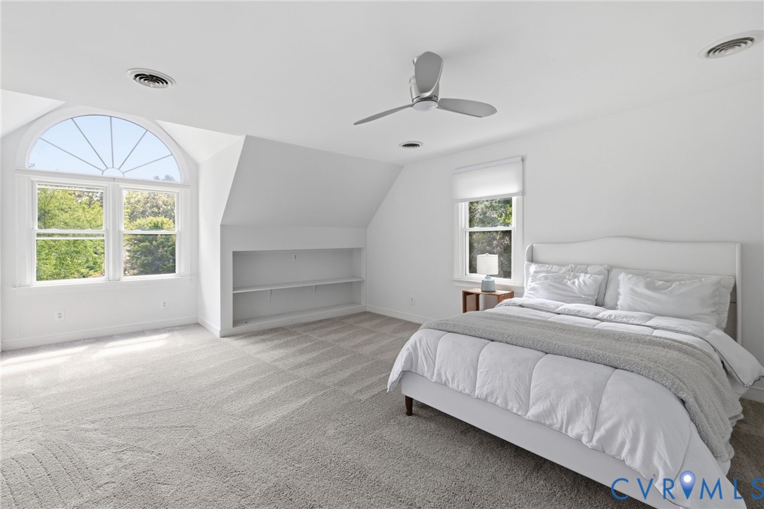Arched window with upper transom, built-in shelving, sloped ceiling, recessed lighting, and ceiling fan