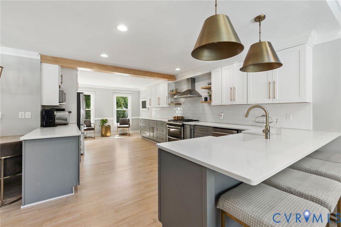Kitchen featuring light wood-finish flooring, two-tone cabinetry, a substantial island with seating, pendant lighting, and stainless steel appliances
