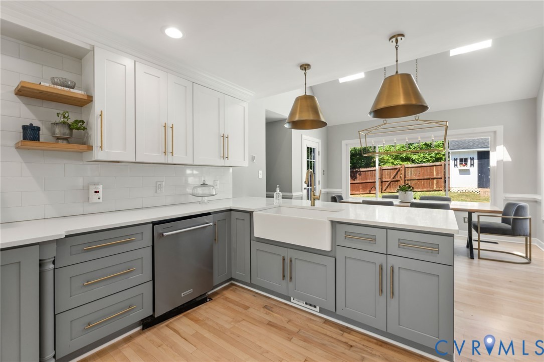 Updated kitchen featuring two-tone cabinetry, stainless steel appliances, a farmhouse sink, and wood-finish flooring
