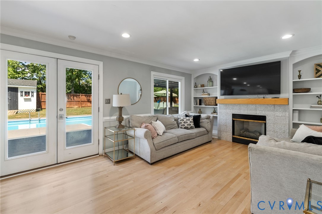 Hardwood flooring, French doors with direct outdoor access, built-in shelving, a fireplace with a stone surround, and recessed lighting