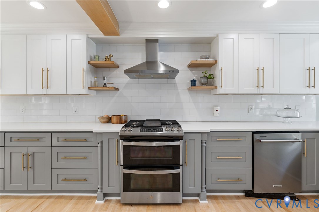 Kitchen featuring two-tone cabinetry, stainless steel appliances, white subway tile backsplash, light-toned countertops, and wood-finish flooring