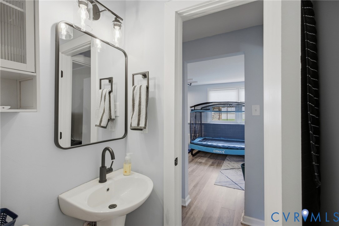 Pedestal sink with a matte black faucet, framed vanity mirror, wall-mounted light fixture, and built-in cabinet storage