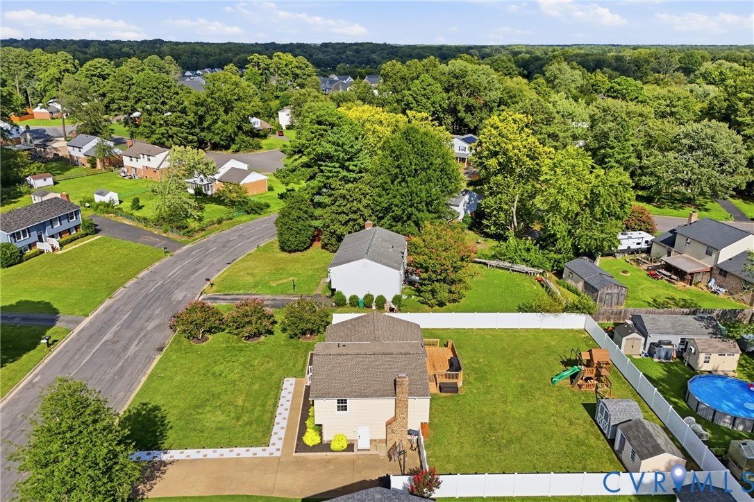 Expansive fenced backyard with a wood deck, multiple storage sheds, and a paved patio area