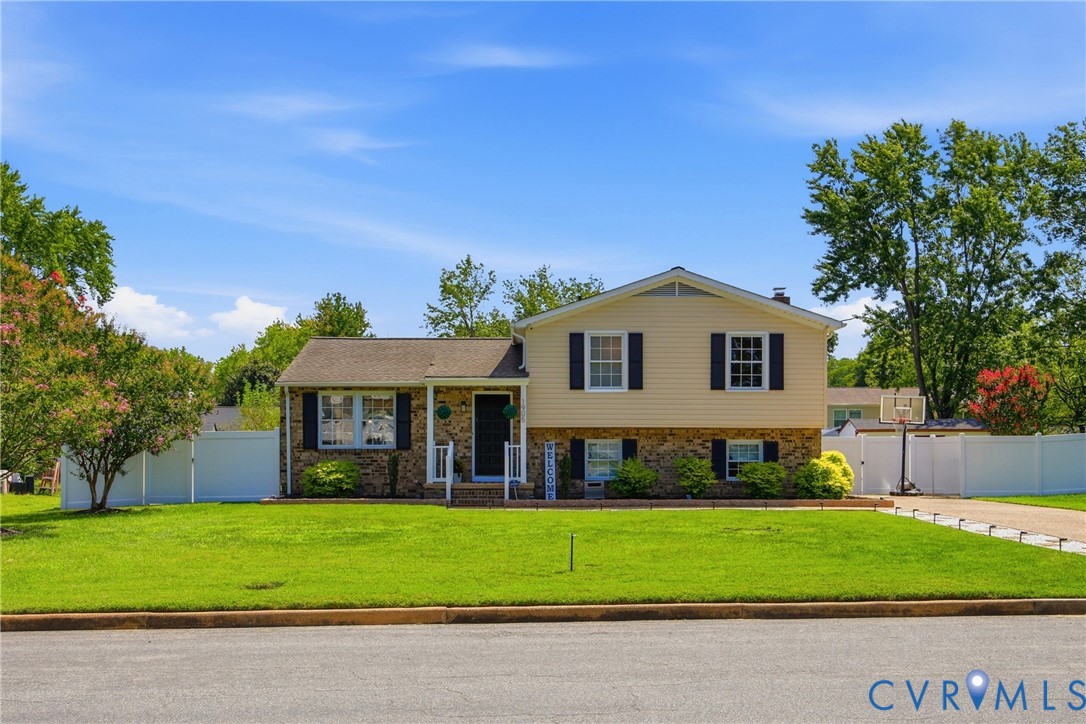 Split-level residence featuring a brick and siding exterior, front porch, mature landscaping, and an extended driveway