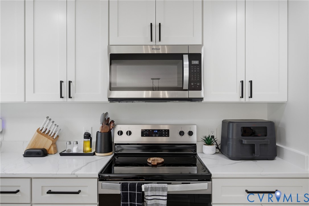 White shaker-style cabinetry with matte black hardware, stainless steel over-the-range microwave, electric range, and light-toned countertops