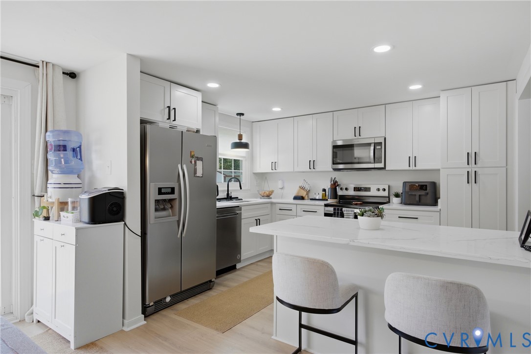 White shaker cabinetry with black hardware, stainless steel appliances, recessed lighting, wood-finish flooring, and a white countertop island