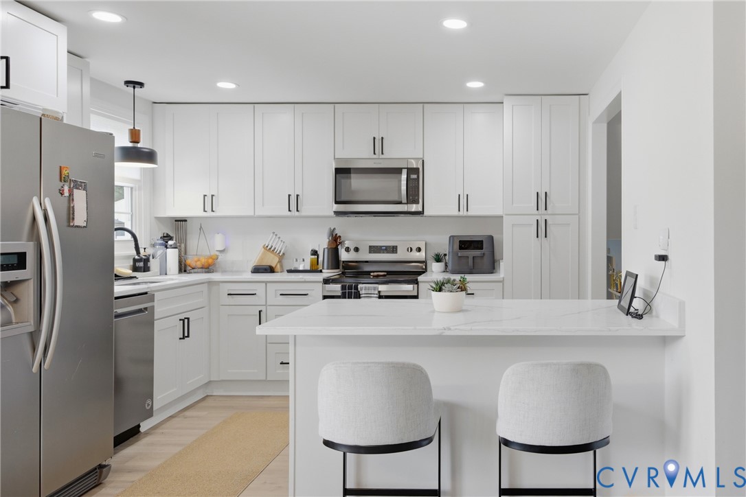 Kitchen featuring white shaker-style cabinetry, stainless steel appliances, recessed lighting, and a white countertop with a breakfast bar