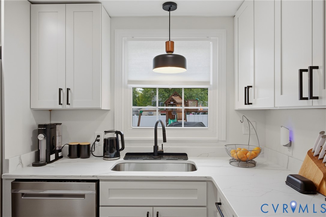 White shaker cabinetry with matte black hardware, stainless steel sink with a gooseneck faucet, light-toned countertops, and a stainless steel dishwasher