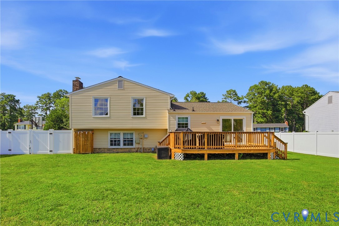 Expansive backyard featuring a manicured lawn, a large wood deck with railings, vinyl siding, and a white privacy fence