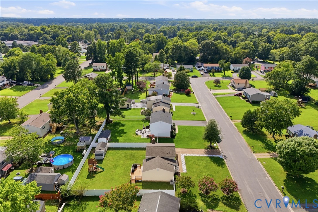 Residential streetscape featuring single-story homes, expansive green lawns, mature trees, and paved roadways