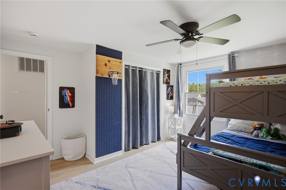 Recessed window with white trim, wood-finish flooring, ceiling fan with integrated lighting, and a built-in wall feature with a textured blue panel