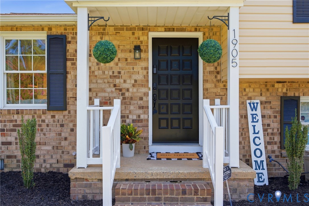 Brick exterior with white trim, featuring a dark paneled entry door and a white railing on the front steps