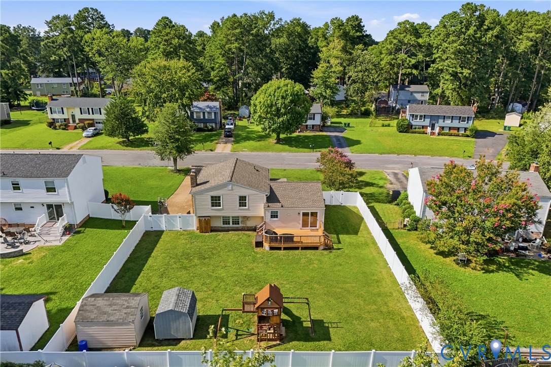 Expansive backyard featuring a manicured lawn, white privacy fencing, and two storage sheds