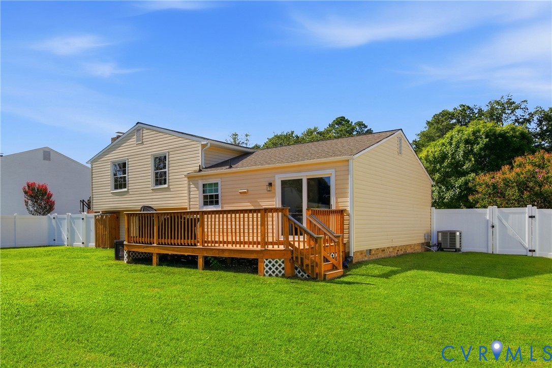 Expansive green lawn featuring a wood deck with railings, vinyl privacy fencing, and sliding glass door access
