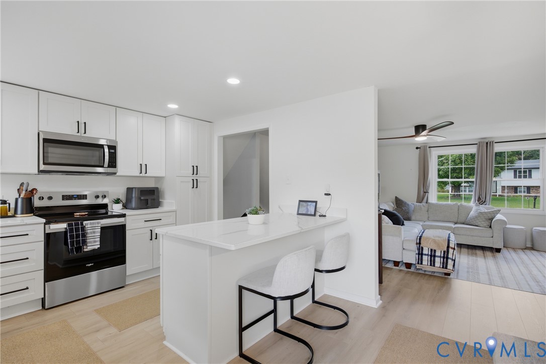 White shaker cabinetry with black hardware, stainless steel appliances, light wood-finish flooring, recessed lighting, and a kitchen island with a white countertop