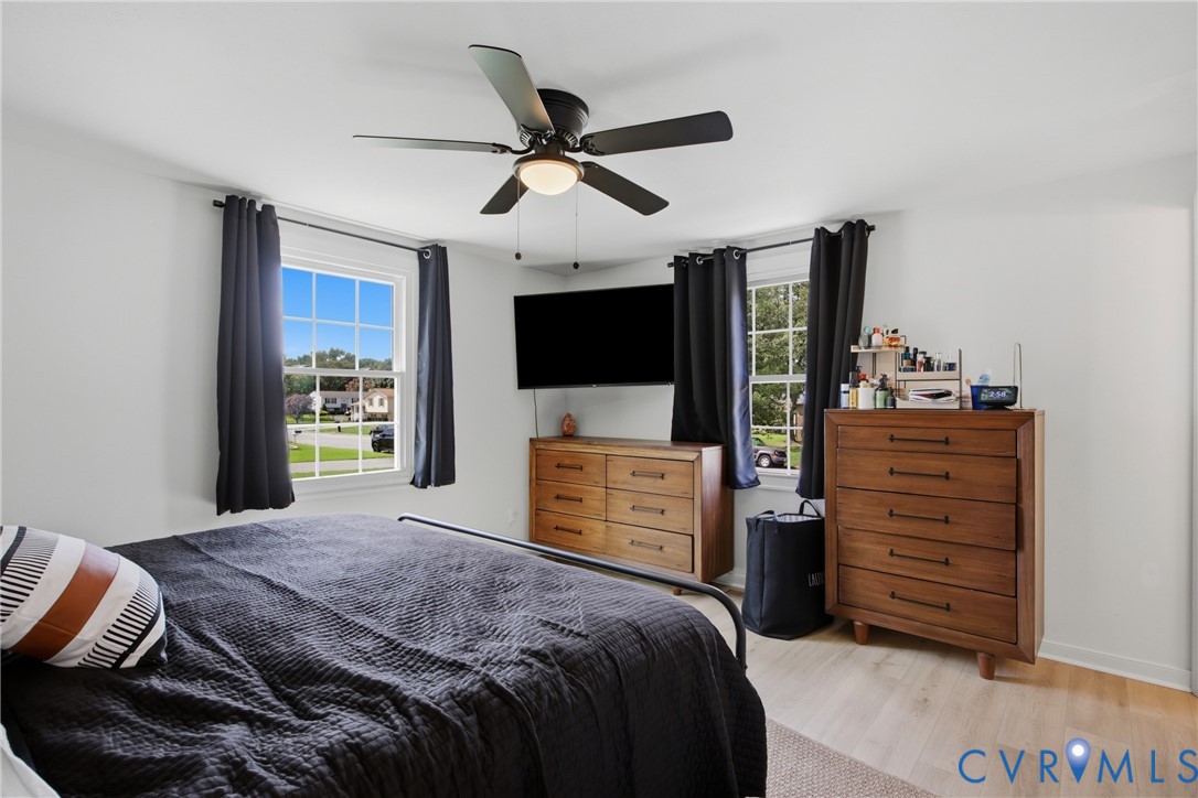 White walls, two windows, ceiling fan with integrated lighting, and wood-finish flooring