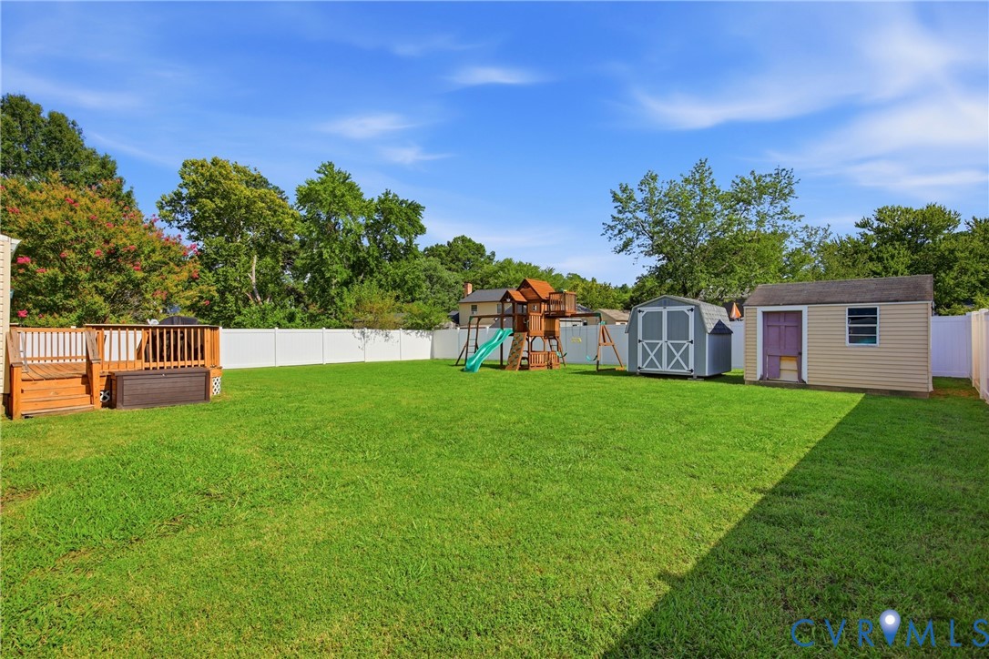 Expansive grassy yard with a white privacy fence, wood-toned deck, and two detached storage sheds