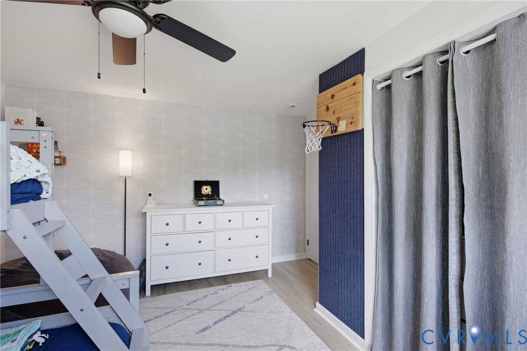Ceiling fan with integrated lighting, wood-finish flooring, accent wall, light-toned wall covering, and a white dresser with dark hardware