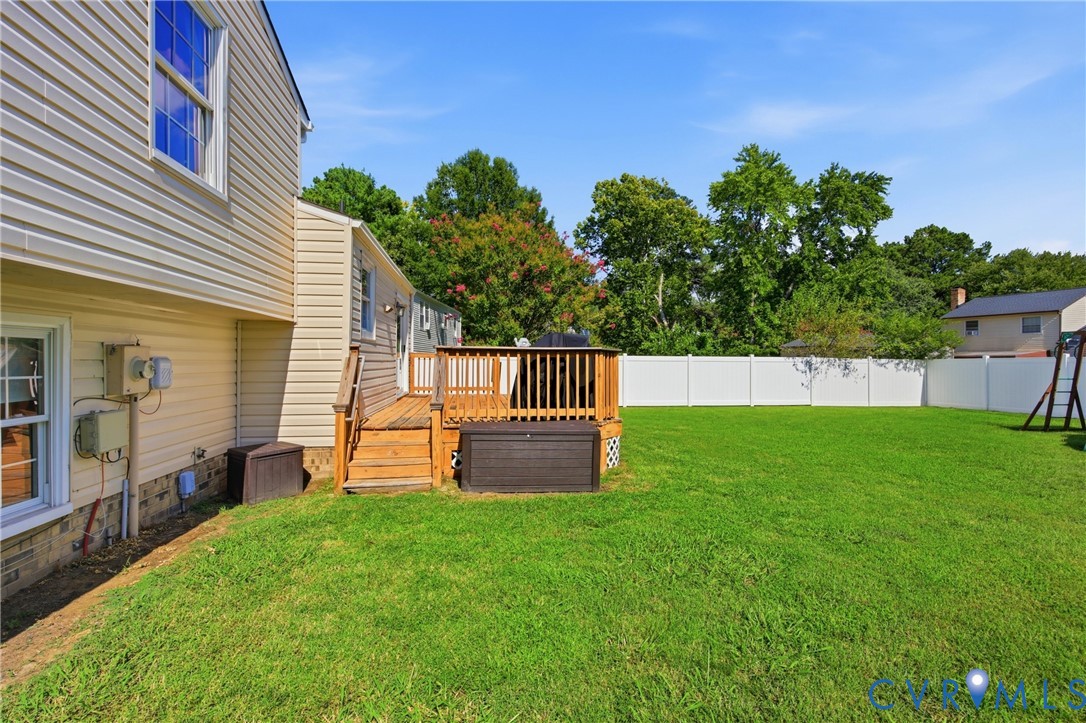 Expansive green lawn, wood-finish deck with railings, privacy fencing, vinyl siding exterior