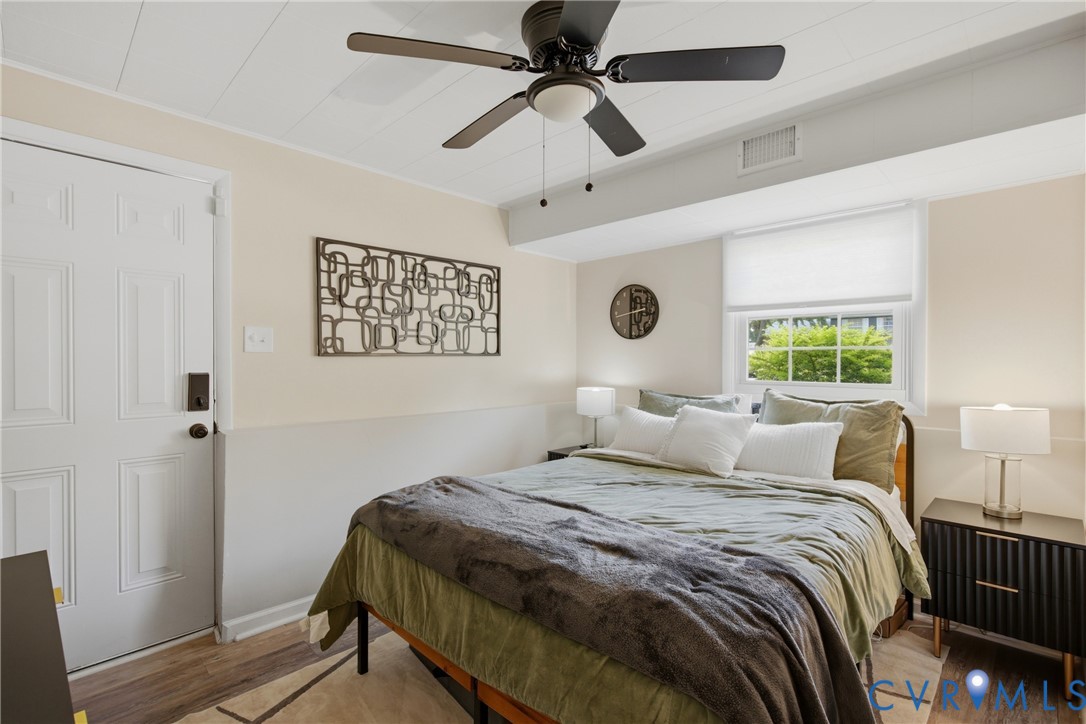 Wood-finish flooring, white paneled door, ceiling fan with integrated lighting, window with roller shade, and built-in wall trim