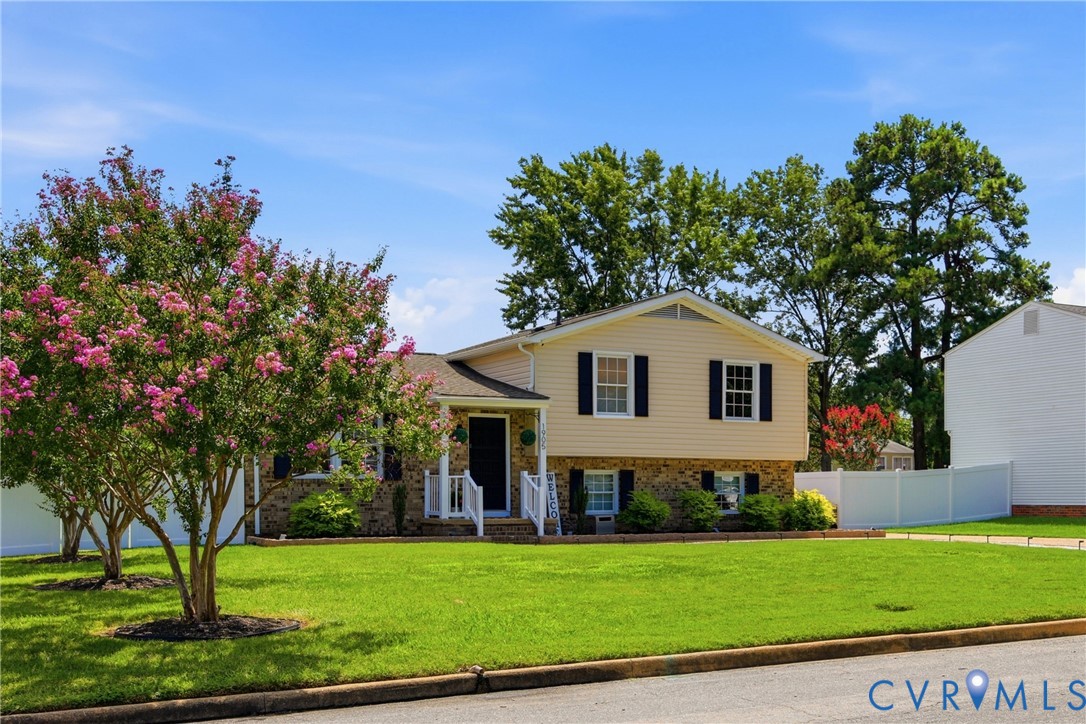 Split-level residence featuring a stone and siding exterior, front lawn, mature flowering trees, and a white picket fence