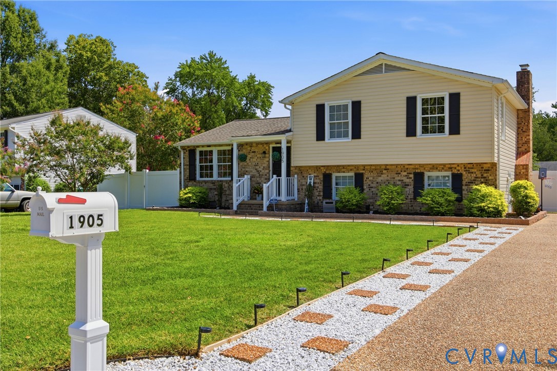 Split-level residence featuring a brick and siding exterior, front porch with white railing, and a gravel driveway