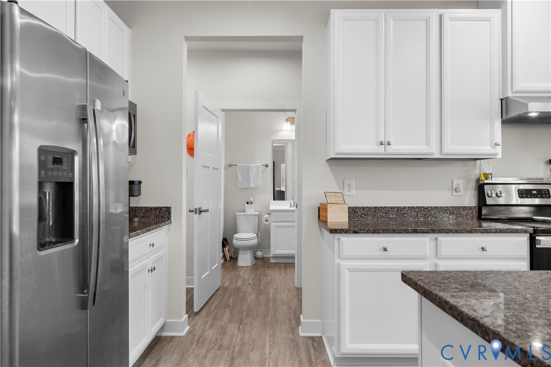 White cabinetry with dark countertops, stainless steel refrigerator, and wood-finish flooring