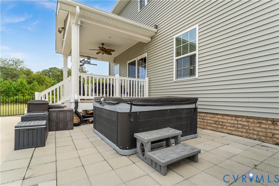 Paved patio featuring a hot tub with steps, covered porch with a ceiling fan, white railings, and siding exterior